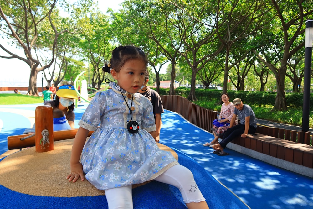 girl in white and blue dress sitting on blue plastic chair