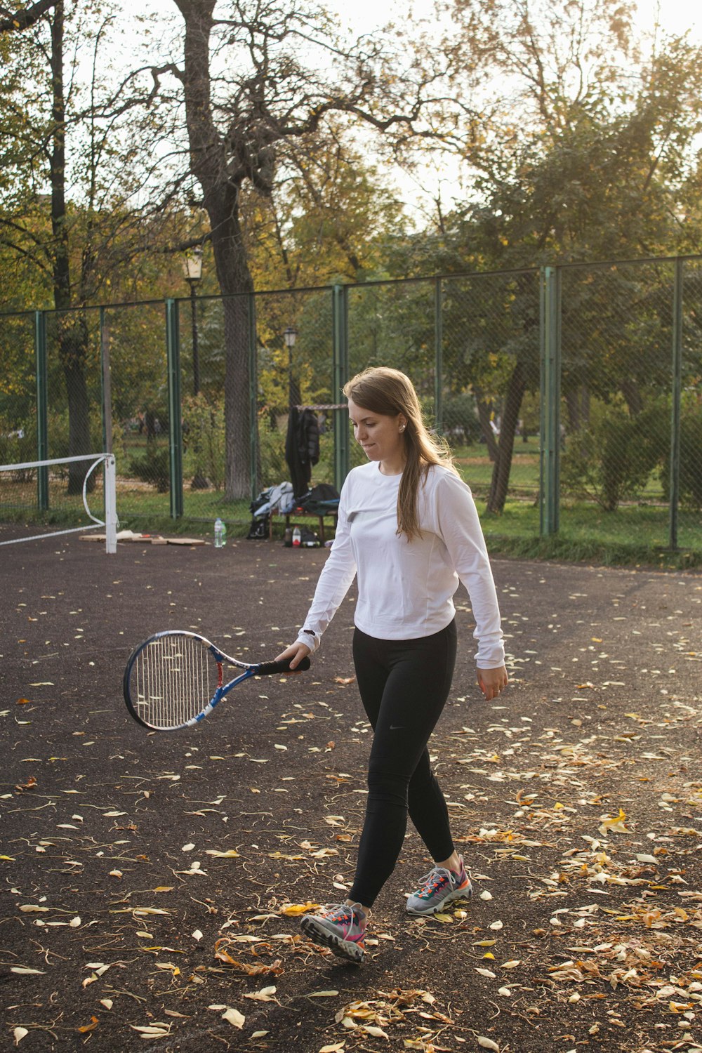woman in white long sleeve shirt and black pants holding tennis racket