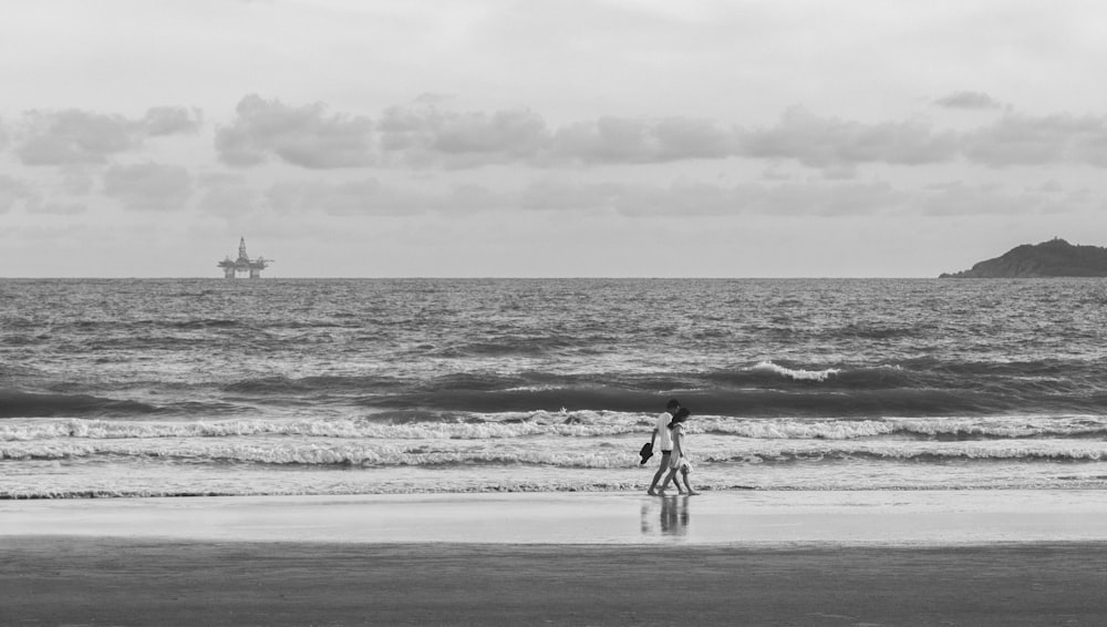 grayscale photo of man and woman walking on beach