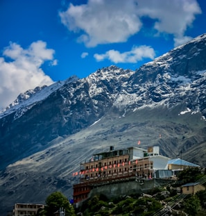brown and white concrete building near snow covered mountain under blue sky during daytime