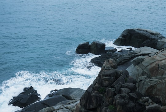 rocky shore with ocean waves crashing on rocks during daytime in Sanya China