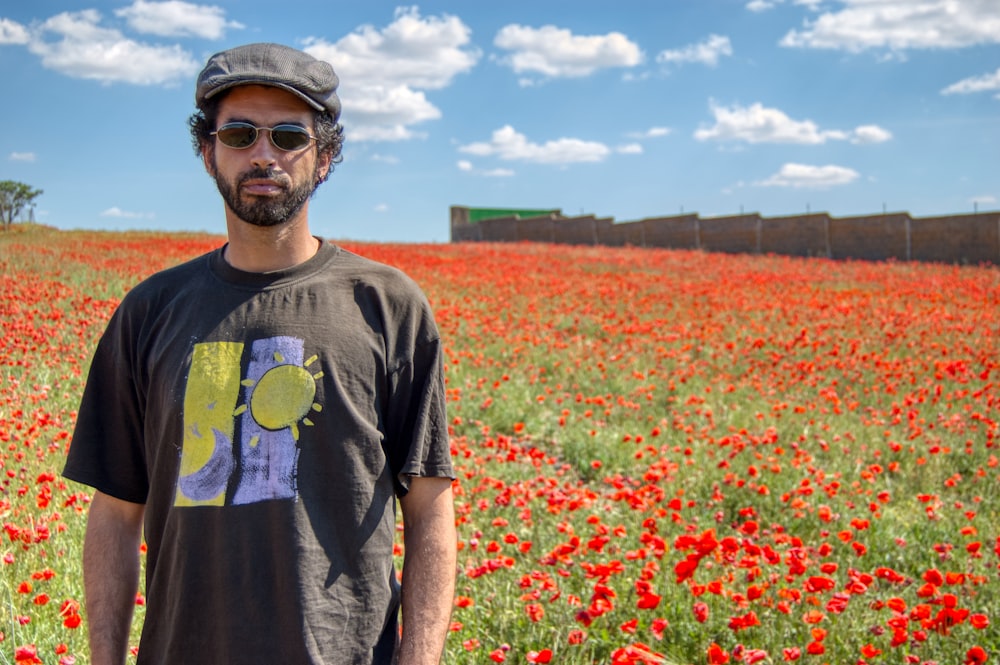 uomo in maglietta girocollo grigia in piedi sul campo di fiori rossi durante il giorno