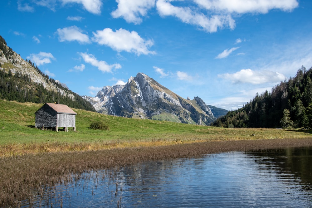 white and brown house near lake and green grass field and mountain under blue sky and