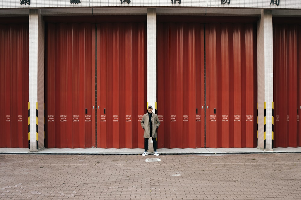 man in black jacket and black pants standing in front of red wall