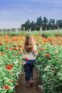 woman in white long sleeve shirt and blue denim jeans standing on red flower field during