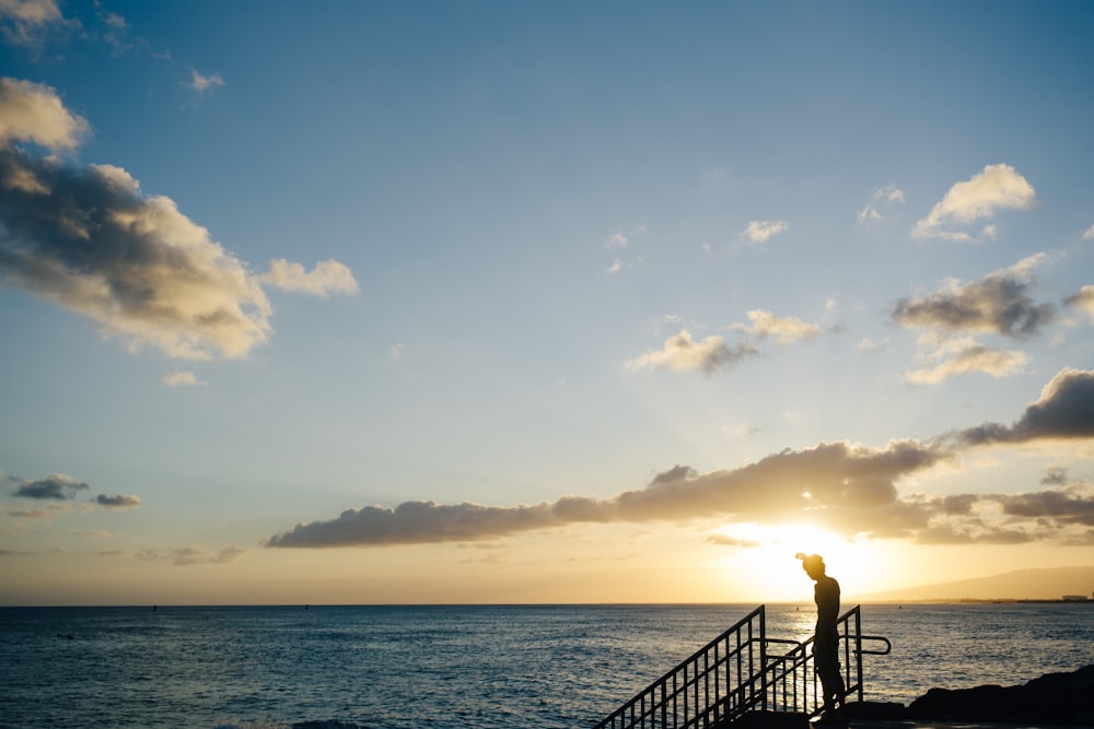 homme debout sur des balustrades en métal noir près de la mer pendant la journée