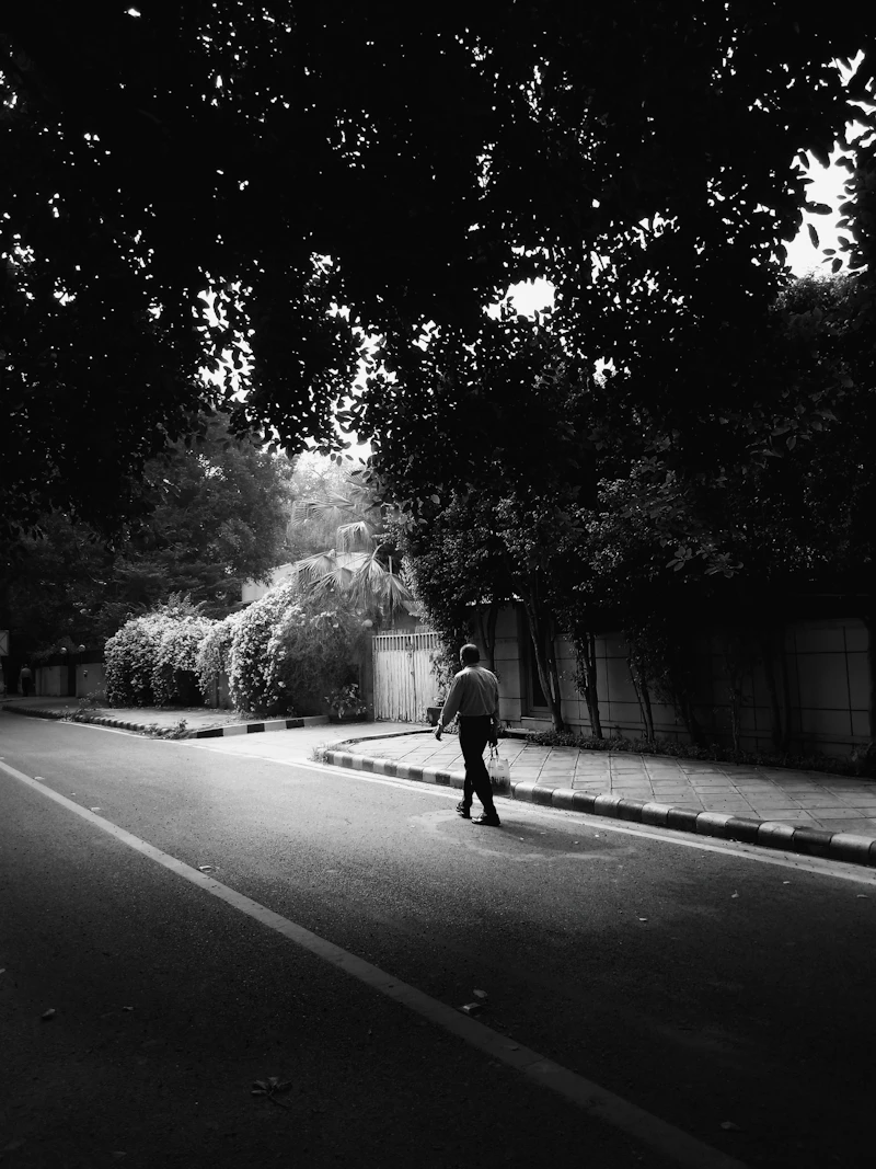 Person walking along a sunlit road, monochrome