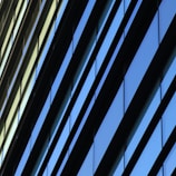 Diagonal lines of glass windows on a modern building create a geometric pattern with alternating hues of blue and beige.