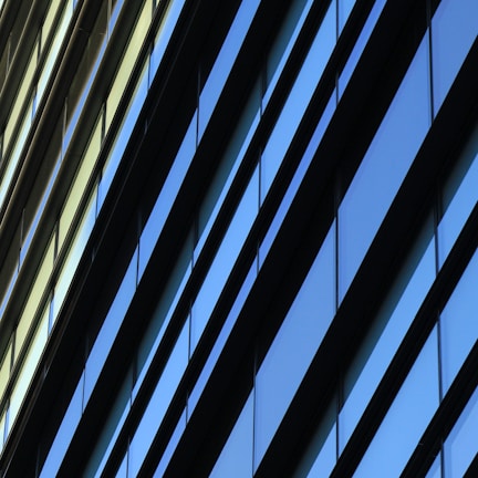 Diagonal lines of glass windows on a modern building create a geometric pattern with alternating hues of blue and beige.