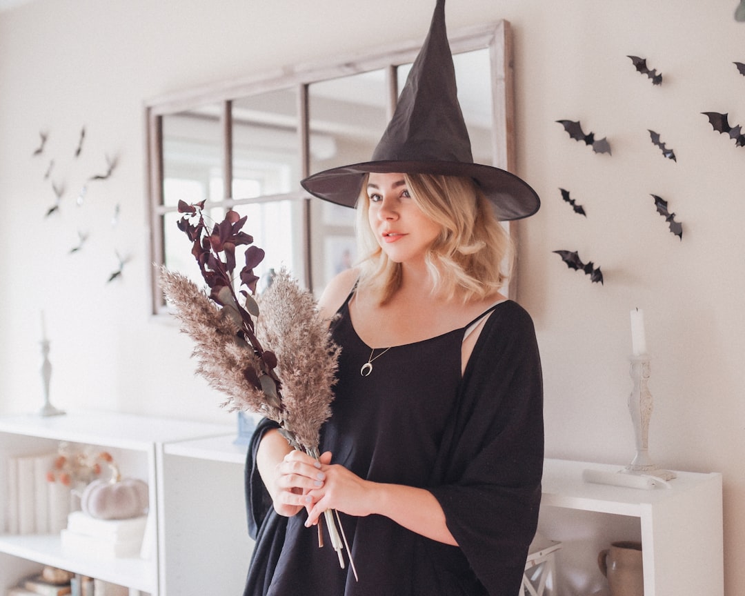 woman in witch hat and black clothing with bats behind her