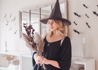 woman in black v neck long sleeve shirt and black hat standing near white wall