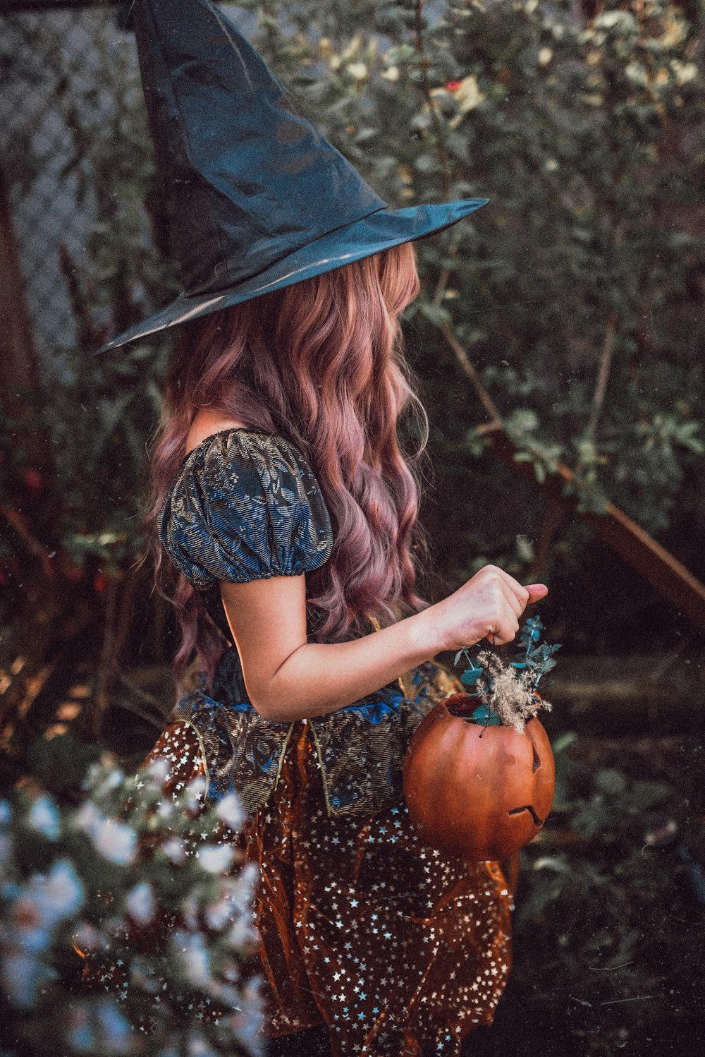 Femme au chapeau noir et robe marron tenant une citrouille