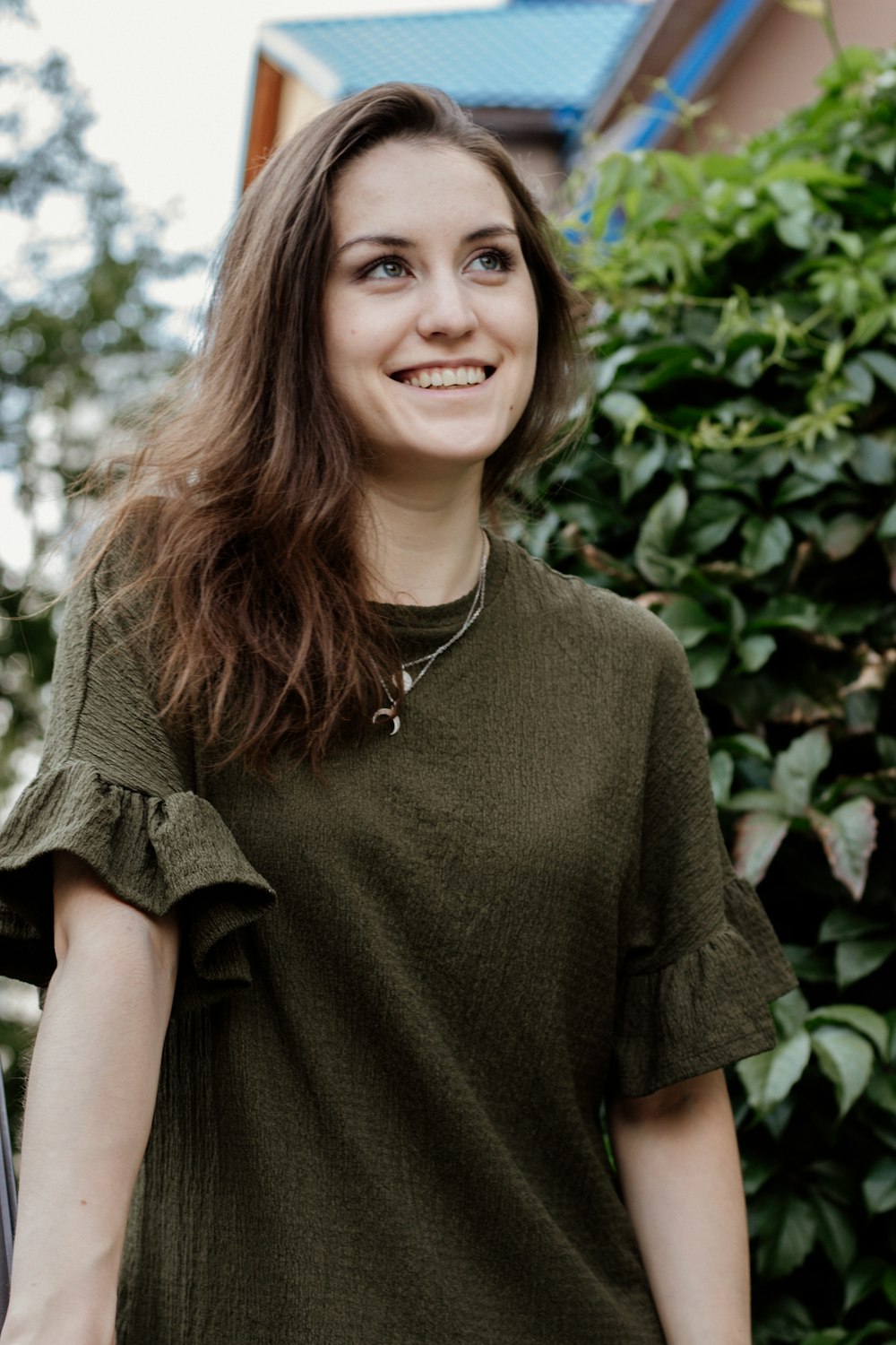 昼間、緑の葉の木のそばに立つ緑のクルーネックTシャツを着た笑顔の女性