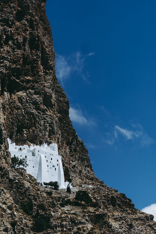 white concrete building on rocky mountain under blue sky during daytime in Amorgos Monastery Greece