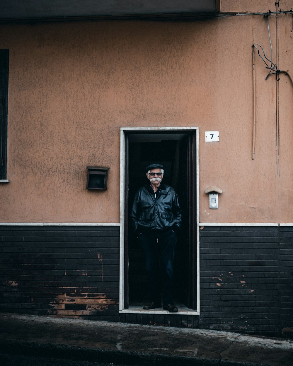 man in black leather jacket standing beside brown wooden door