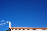 A roof with red tiles is visible under a clear blue sky. Several white cables or wires extend from a corner chimney, adding geometric lines to the scene.