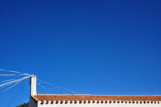 A roof with red tiles is visible under a clear blue sky. Several white cables or wires extend from a corner chimney, adding geometric lines to the scene.