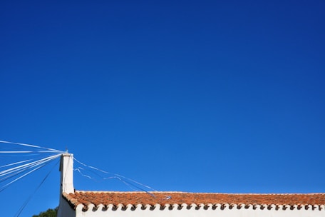 A roof with red tiles is visible under a clear blue sky. Several white cables or wires extend from a corner chimney, adding geometric lines to the scene.