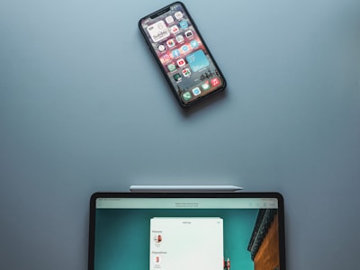 A smartphone with various app icons is placed above a tablet with a stylus resting on its edge. The tablet screen displays an application interface with options.