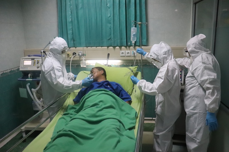 A hospital scene with a patient in bed and healthcare workers in protective gear attending to them.