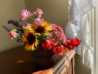 A wide mouth ceramic vase filled with fresh wildflowers on a sunlit windowsill.