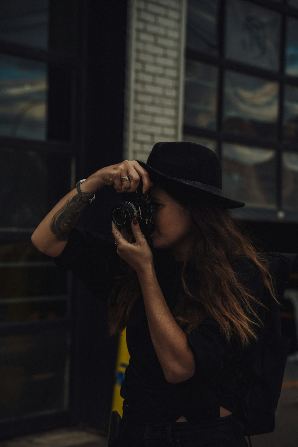 woman in yellow tank top wearing black fedora hat holding black dslr camera