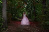 A model dressed in avant-garde fashion, posing in a lush green forest.