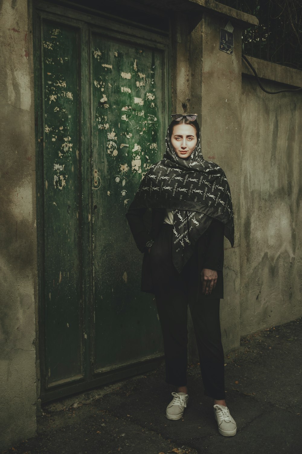 woman in black and white hijab standing beside green wooden door