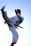 A person in a white martial arts gi executing a high kick against a clear blue sky. The figure is in mid-air, showcasing a dynamic and powerful pose, with movement captured in the focus.
