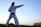 A person wearing a traditional martial arts uniform with a black belt stands in a stance, poised with one arm extended in a punch. The background features an open sky transitioning from light to deep blue, suggesting early evening or dawn. The ground is grassy, and some foliage is visible.