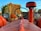 A red tractor is prominently featured in the foreground, with a round steering wheel centered above the body. On either side of the tractor, large circular headlights are visible. In the background, a stack of hay bales is decorated with pumpkins and corn stalks. A sign for 'Kat Acres Farm' is partially visible, adding an autumnal farm setting.