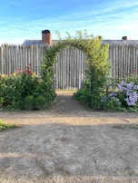 A charming wooden garden arbor framing a blooming rose pathway under a clear blue sky.