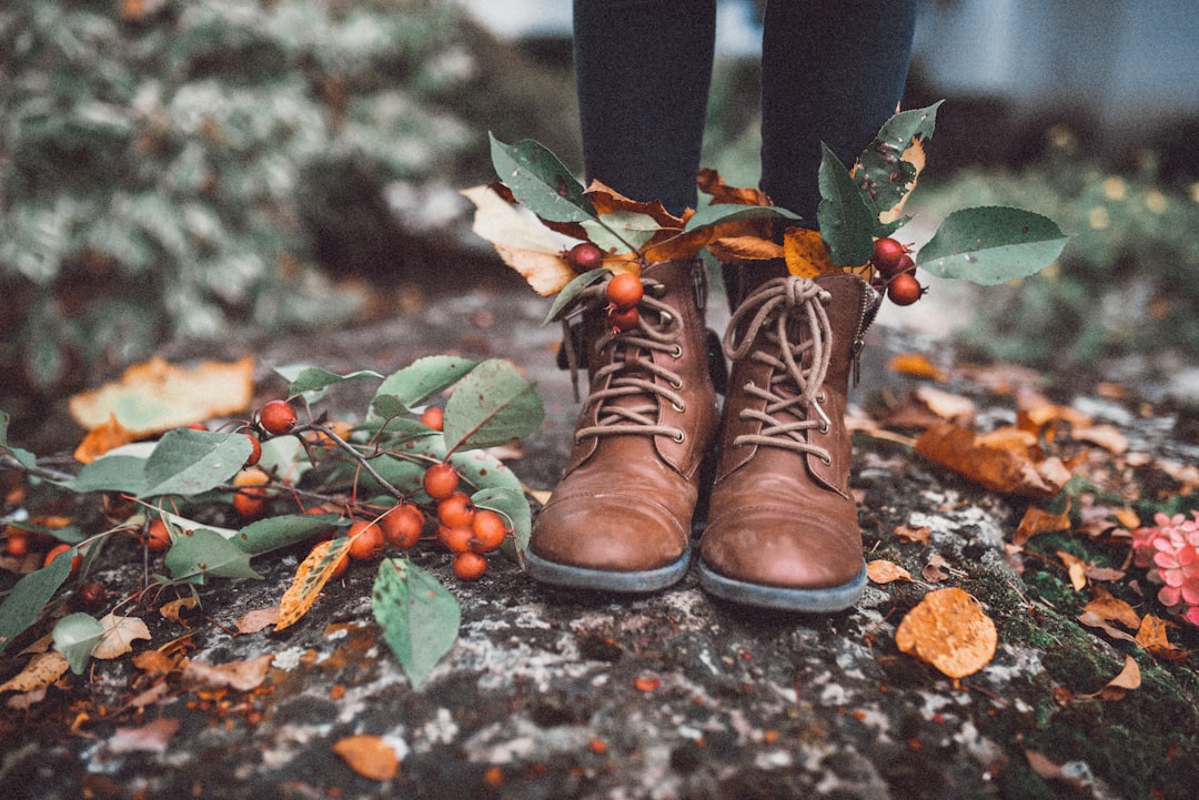 person wearing brown leather boots standing on ground with green leaves
