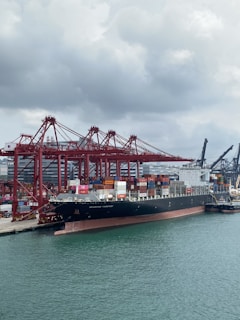 Cargo ship docked at port with containers and cranes in the background
