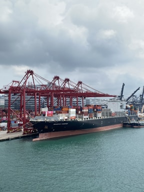 Cargo ship docked at port with containers and cranes in the background