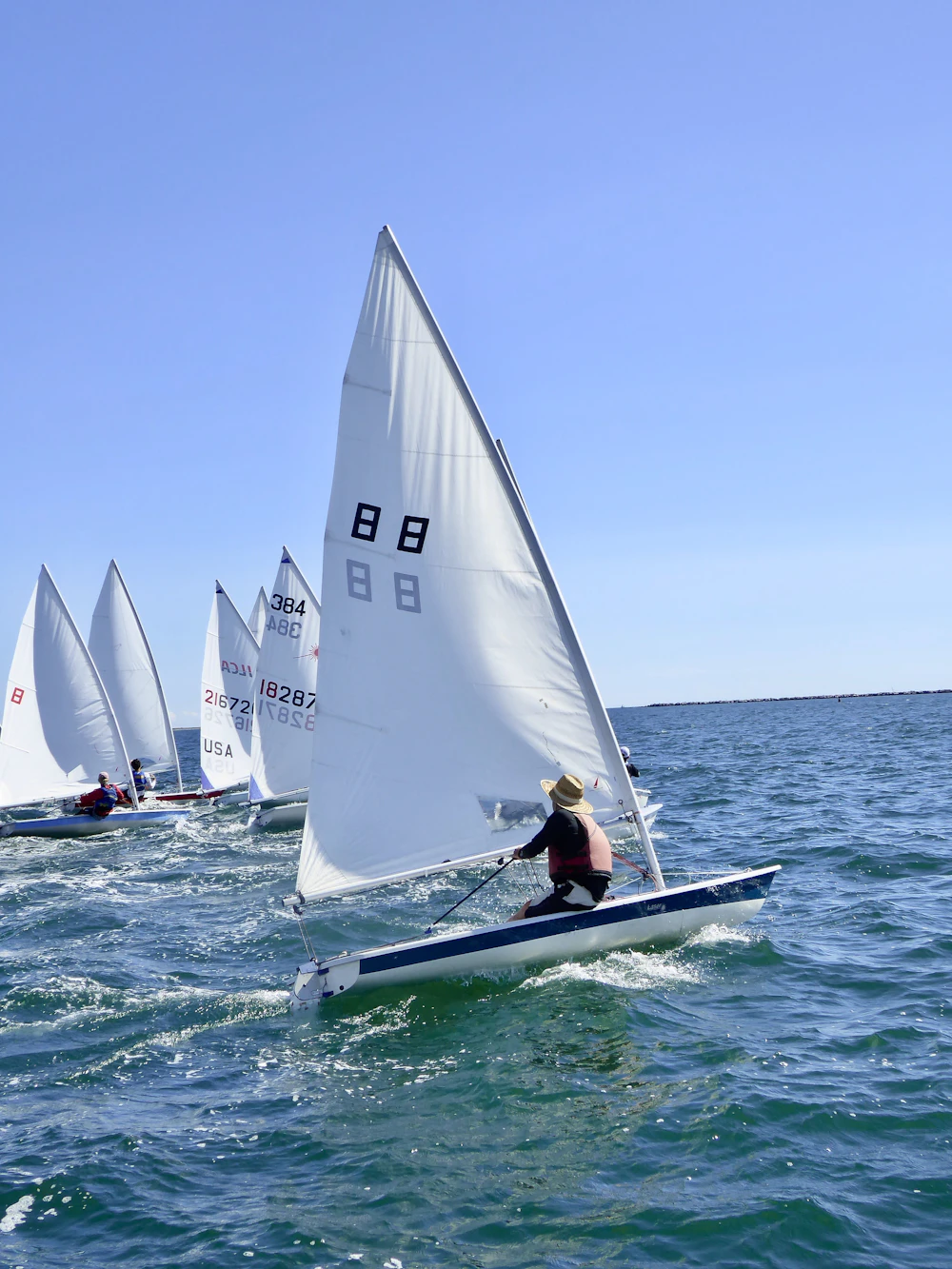 Two small singlehanded training dinghies with sail numbers on blue water
