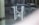 A chain and padlock secure metal handles on a glass door, with a reflection of a parked car and street scene visible in the background. The atmosphere appears quiet and subdued.