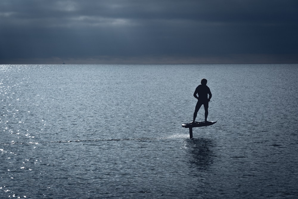 uomo in muta umida nera in piedi su paddle board di legno marrone durante il giorno
