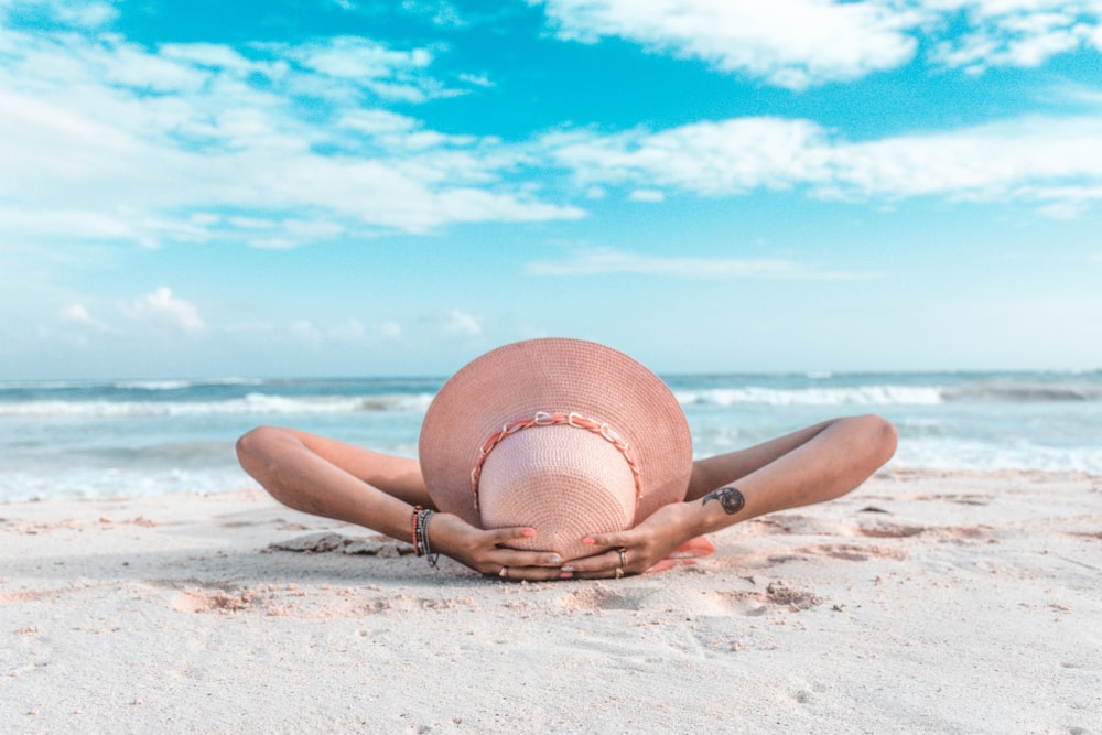 Frau mit braunem Sonnenhut liegt tagsüber auf Sand