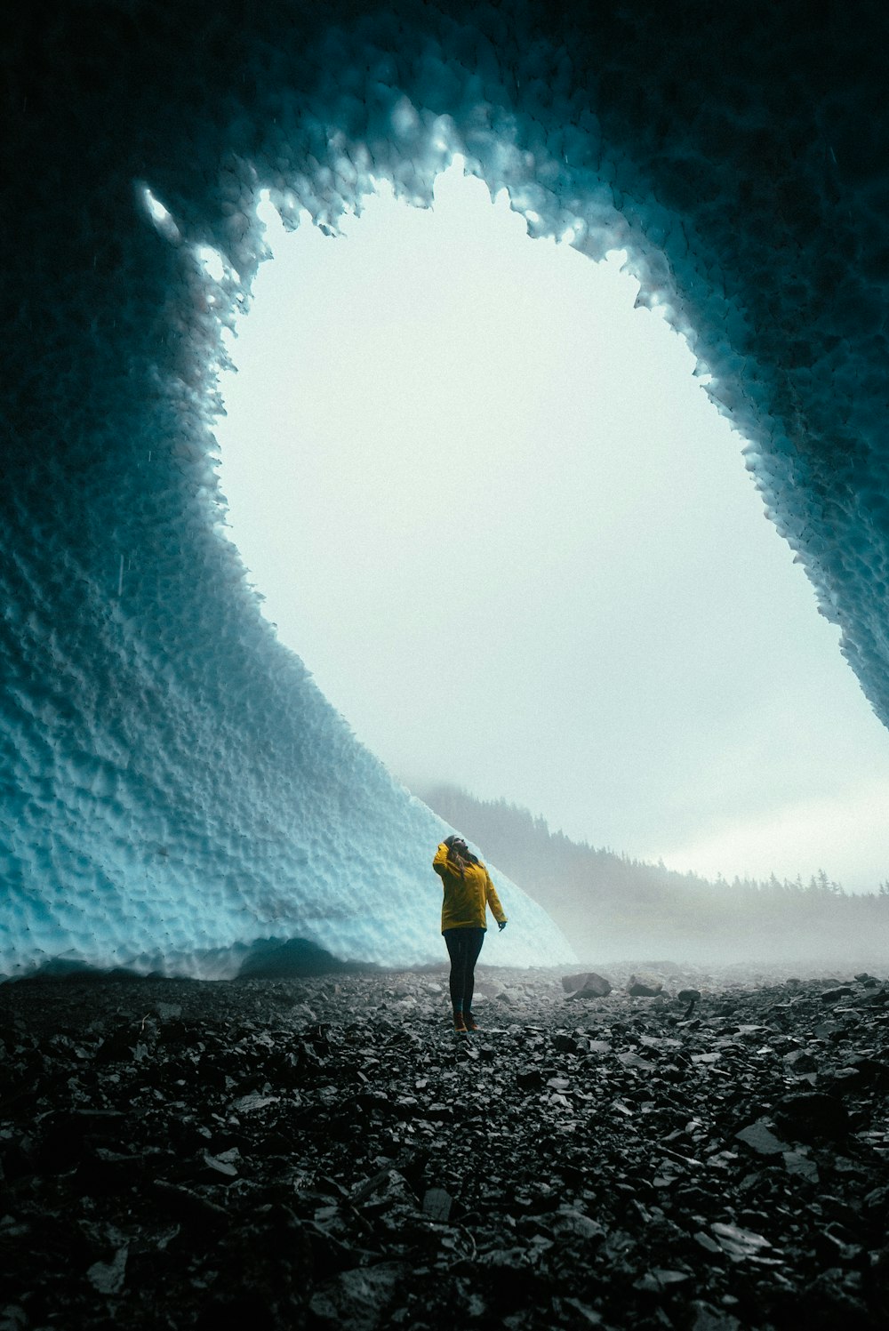 person in yellow jacket and black pants standing on rocky ground during daytime