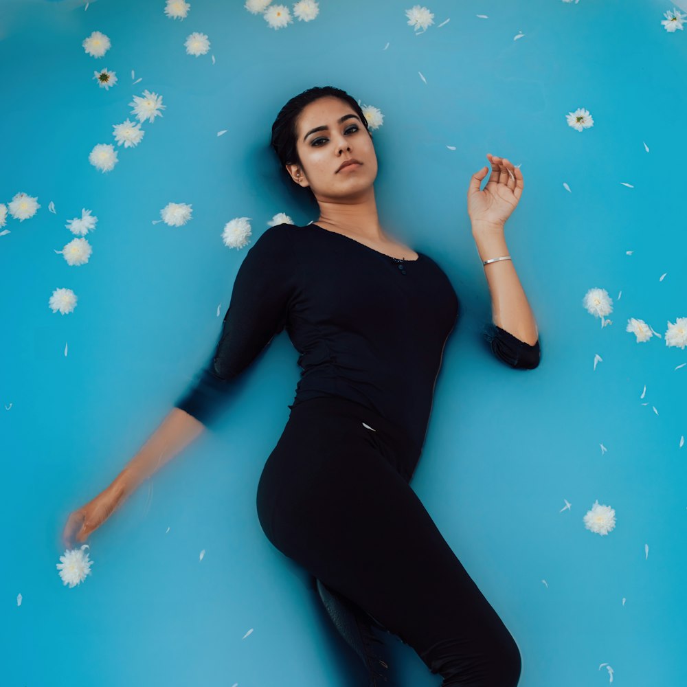 woman in black long sleeve shirt and black pants lying on blue and white floor
