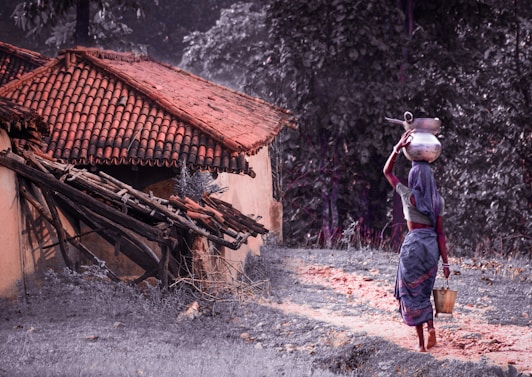 man in blue denim jacket and blue denim jeans standing near brown wooden house during daytime