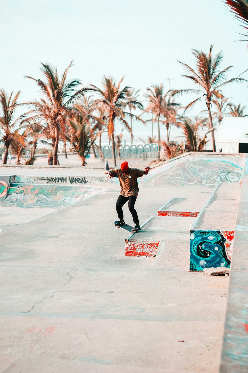 Uomo in giacca rossa e pantaloni neri che gioca skateboard sulla strada di cemento grigia durante il giorno