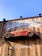 A red vintage car is affixed to a wooden wall, seemingly defying gravity. The wall bears the words 'Dependable' and 'Auto Repair' in large white letters. The car is an old model and has the phrase 'Mechanic on Duty' written on its side.