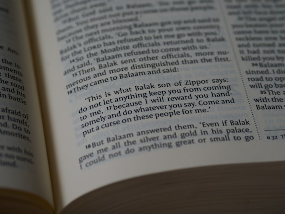 A close-up view of an open book showing a biblical text. The passage features quotes from Balak son of Zippor and Balaam.