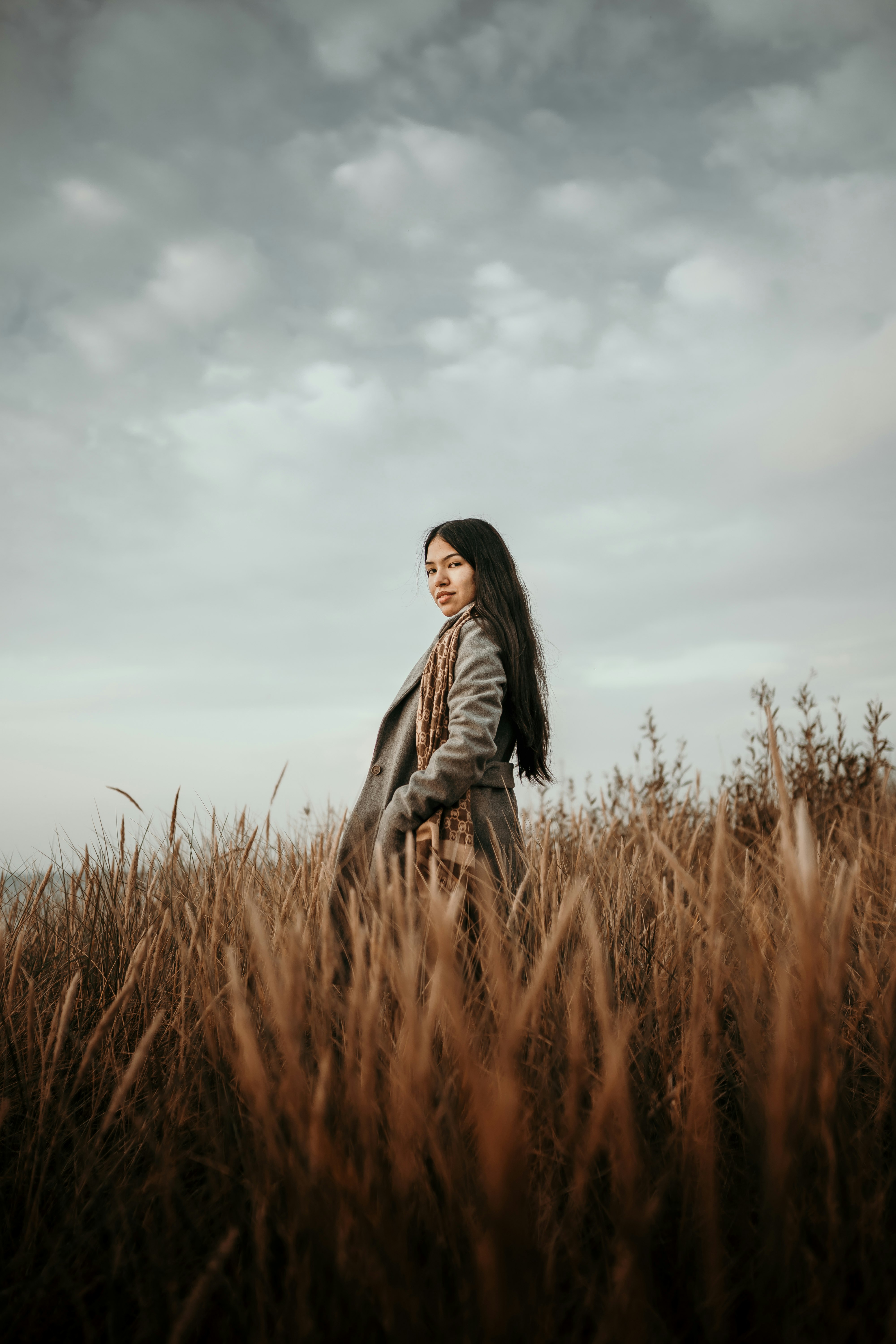 woman in black leather jacket standing on brown grass field under white clouds during daytime