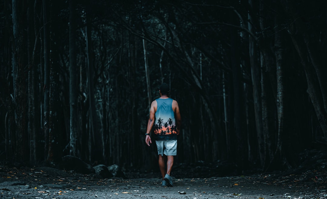 man in blue tank top and blue denim shorts standing in the middle of the forest