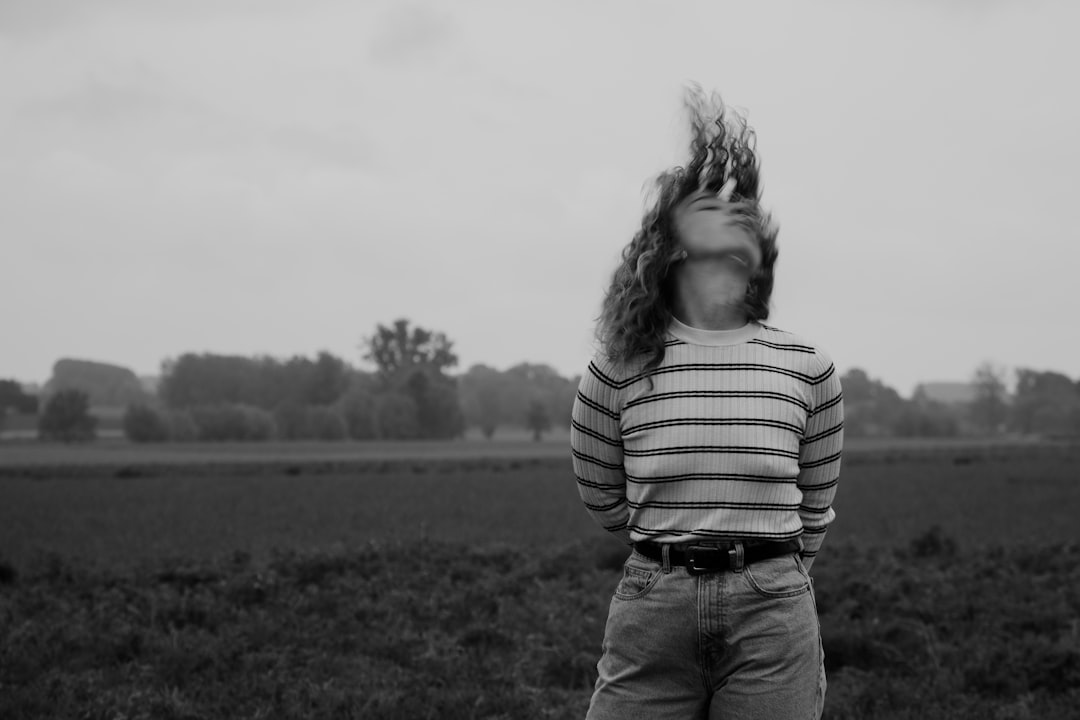 grayscale photo of girl in striped long sleeve shirt and denim jeans standing on grass field