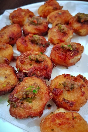 Golden brown, fried pieces of food topped with green and red garnishes are arranged on a paper towel-lined plate.