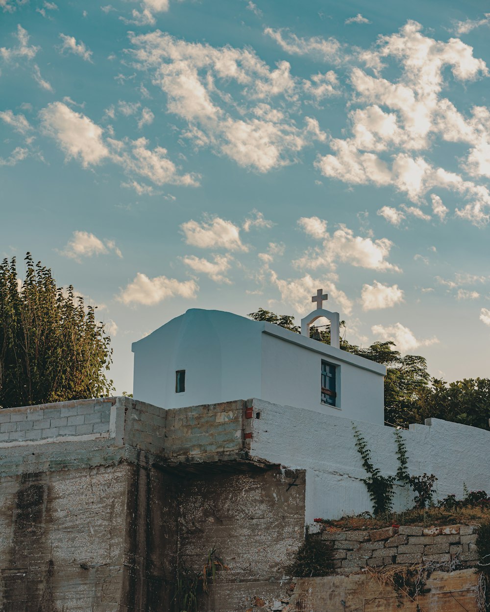 white concrete building near green trees under blue sky and white clouds during daytime